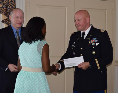 Soldier in dress uniform shakes hand of young woman at award ceremony.
