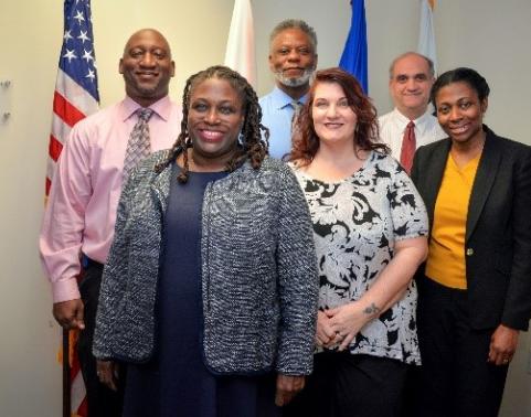 DCATS Cyber Team stands together, in front of flags.