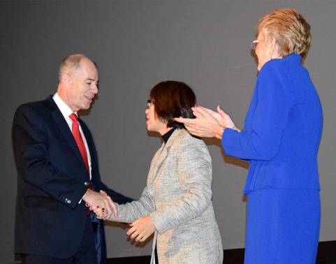 Man shakes hand with woman on stage during a ceremony