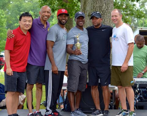 Photo: Six men in athletic wear stand on outdoor stage while one holds a trophy.