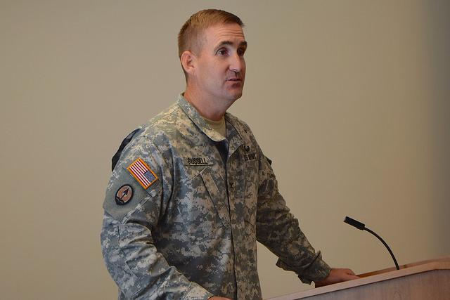 Col William Russell addresses crowd from behind podium.