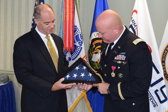 Two men hold folded framed flag.