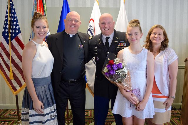 Pastor, man, woman and two young girls pose for picture in front of flags.