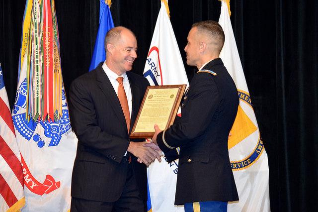 Two men shake hands while holding framed certificate.