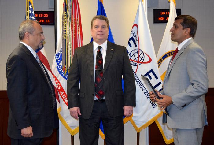 Three men stand in front of flags during ceremony.