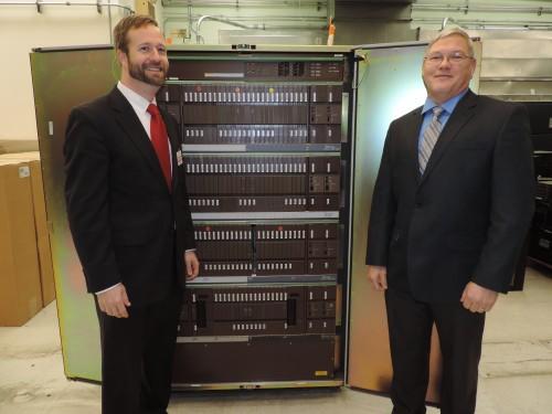 Two men stand beside old telephone system.