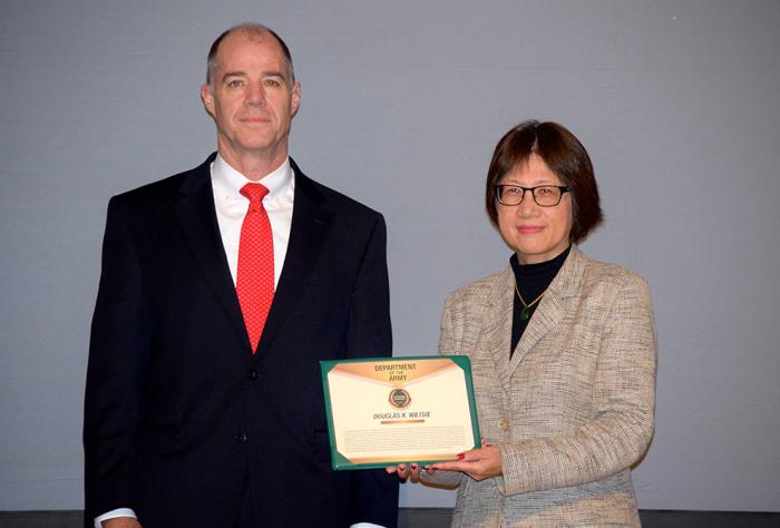 Two people standing next to one another. One person holds framed certificate.